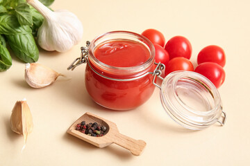 Jar of tasty tomato sauce with garlic, peppercorns and basil leaves on beige background