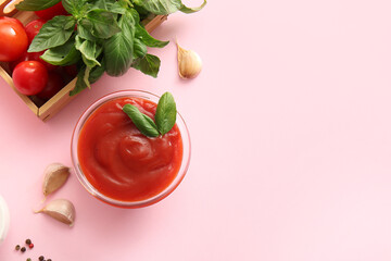 Glass bowl of tasty tomato sauce with basil leaves and garlic on pink background