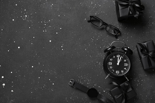 Alarm clock with smartwatch, eyeglasses and gifts on dark background. Cyber Monday