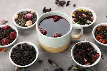 Bowls with different fruit tea and cup of brewed beverage on grey grunge background
