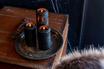 Black candles burning flame on silver platter with old leather trunk
