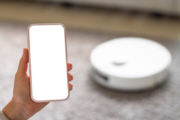 Woman holding smartphone with blank screen near robotic vacuum cleaner at home