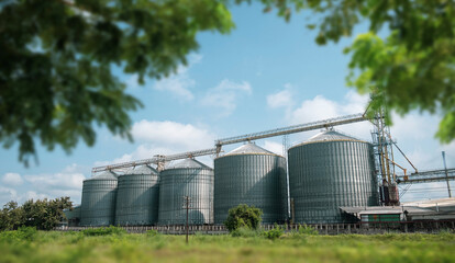 Large metal silos for grain storage at an agricultural processing factory under a bright blue sky....