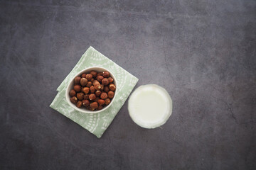 Bowl of hazelnuts and a glass of milk on a textured surface