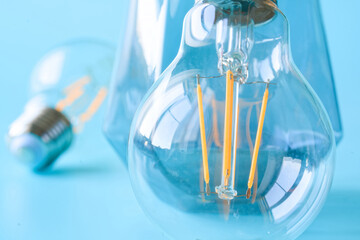 Close-up of modern LED filament light bulb with yellow glowing threads on blue background, concept of innovation and energy efficiency. Macro shot. Photo