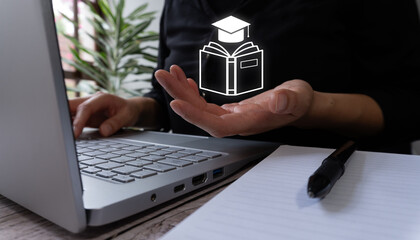 A woman in front of a computer holding a book wearing a graduate cap. Online education