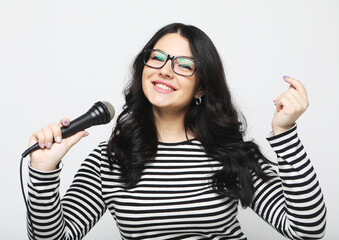 Lifestyle, party and people concept: young woman wearing striped shirt , holding microphone, singing and smiling.