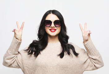 Portrait of young woman wearing sunglasses showing victory sign near face