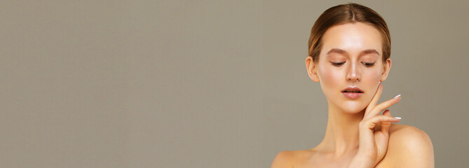 A beautiful young woman with a perfect face touches her facial skin with her fingertips.