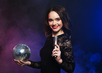Young happy woman in evening dress holding microphone and disco ball.