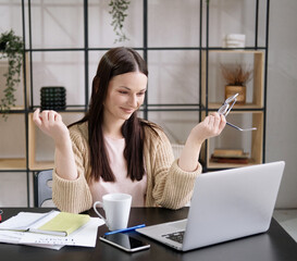 Young cheerful cute beautiful business woman sit indoors in office using laptop computer with headset.