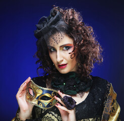 Portrait of smiling woman with artistic make-up holding mask over blue background.