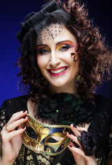Portrait of smiling woman with artistic make-up holding mask over blue background.