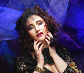 Fashionable woman with creative makeup and hairstyle posing on dark blue background.