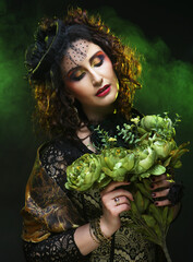 Beautiful woman with bright make up wearing hat with veil holding dry green flowers.