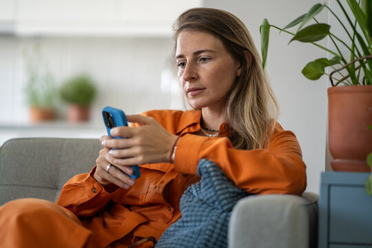 Middle-aged woman deeply focused on phone browsing content with calm, deliberate expression. Female experiencing quiet concentration and relaxation finding enjoyment in information or online shopping
