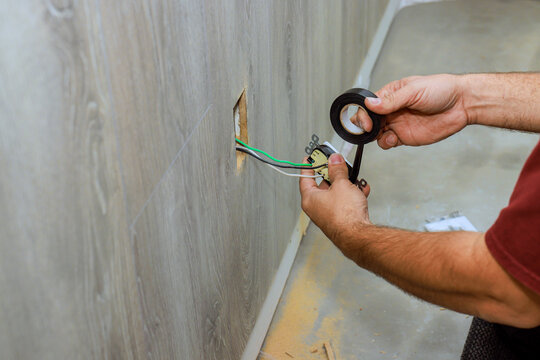 Electrician wraps electrical wires with tape while working on wiring in home renovation.
