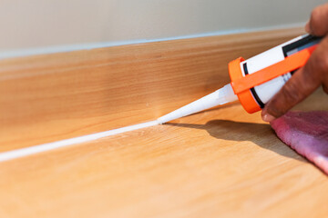 Hand Applying Caulk Sealant to Baseboard Gap