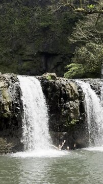 brave girl and man stand under powerful tall waterfall  in dense rainforest next to unique Nandroya Falls, Wooroonooran National Park, Waterfall Way, tropical North Queensland, Cairns, Australia