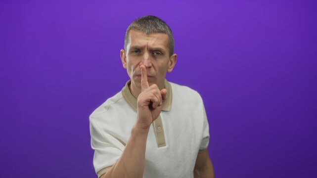 Man gesturing silence with finger on lips against purple background, creating a calm and secluded atmosphere with a caucasian expression in an isolated wall setting.