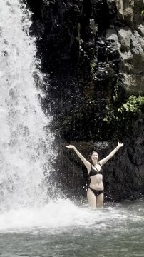 brave girl in bikini stands under powerful tall waterfall  in dense rainforest next to unique Nandroya Falls, Wooroonooran National Park, Waterfall Way, tropical North Queensland, Cairns, Australia