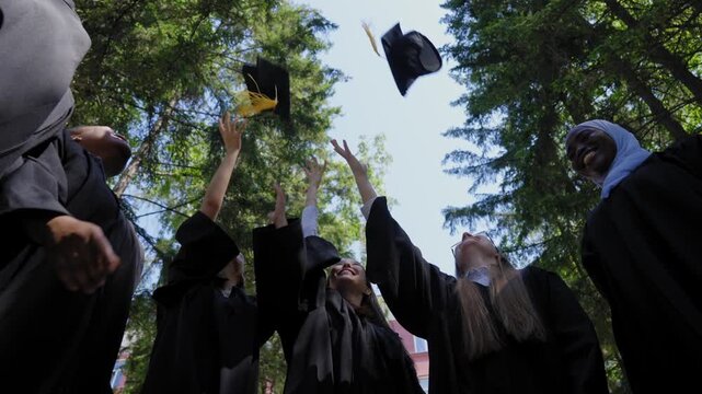 Students of different nationalities in graduation gowns throw their caps in the air. 