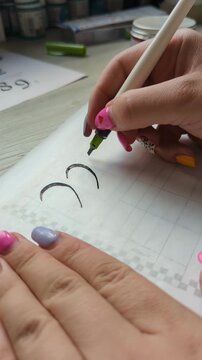 Artistic lettering process with ink pen, focused on handwriting skills. Hand of an artist writing decorative script on paper, demonstrating calligraphy practice and artistic expression.