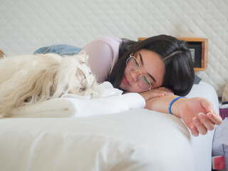 Asian woman relaxing on bed with her Shih Tzu dog in cozy bedroom. Simple happiness and home lifestyle concept.
