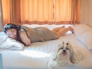 Asian woman relaxing on bed with her Shih Tzu dog in cozy bedroom. Simple happiness and home lifestyle concept.