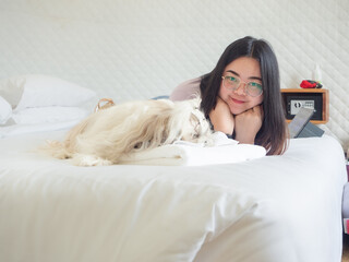 Asian woman relaxing on bed with her Shih Tzu dog in cozy bedroom.
