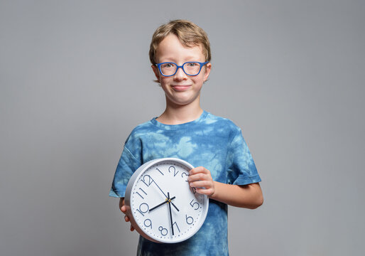 Smiling little boy in glasses holds clock in his hands