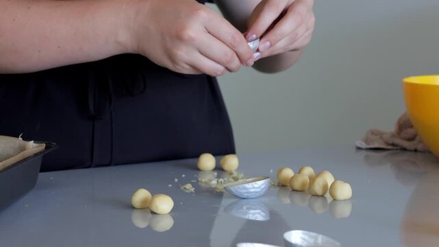 White baker apprentice shaping cookie dough balls on countertop, closeup hands rolling uniform spheres, parchment lined tray and yellow mixing bowl visible, home baking