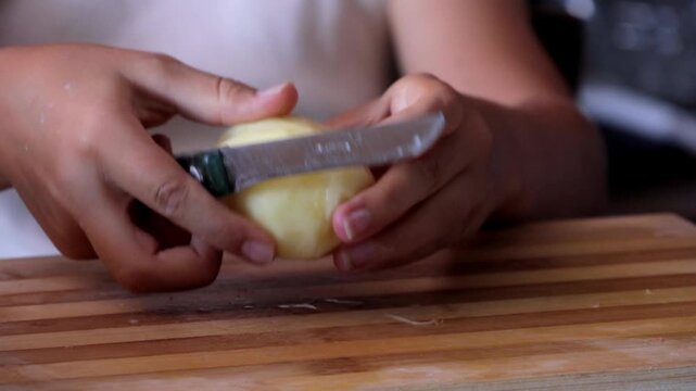 Hand slicing potato, Closeup of hand slicing potato on wooden cutting board, Detailed image of hand expertly slicing peeled potato with small knife and proper technique