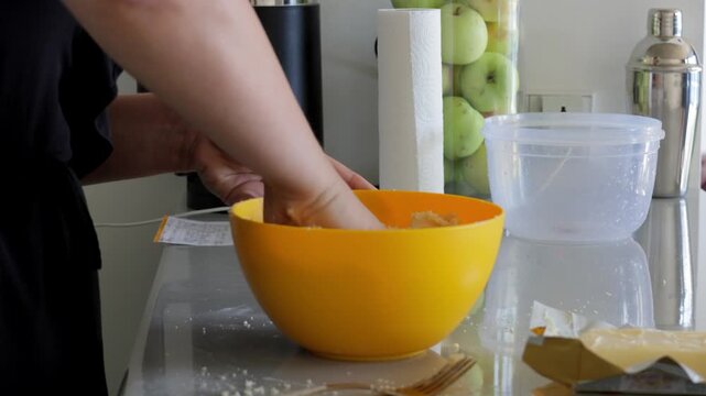 White professional baker combining large dough batch by hand in deep yellow bowl, vigorous mixing and kneading on kitchen worktop, commercial home hybrid setting