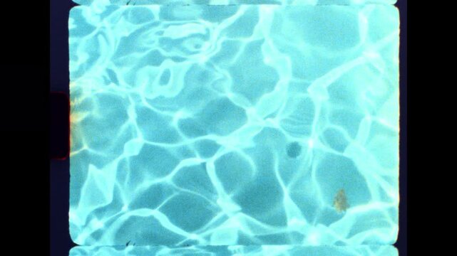 Retro 8mm film look showing clear pool water with sun reflections and a floating leaf on a bright day