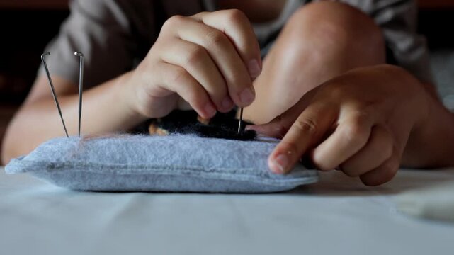 Closeup low angle showing hands felting small animal on cushion with knees visible, intimate relaxed pose, needles upright in pad, domestic studio comfort, slow craft