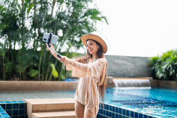 Young Hispanic Gen Z Woman in Swimwear Creating Travel Vlog as Influencer by Resort Pool in Summer