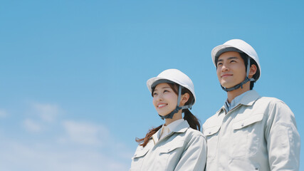 青空の下で笑顔を見せる若手男女の作業員