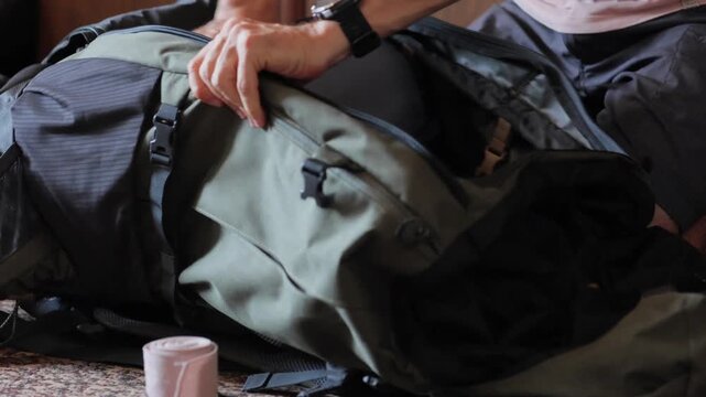 White man packing expedition duffel on carpet, careful hands slotting layers and accessories into inner pocket and adjusting buckles for balanced load before long voyage
