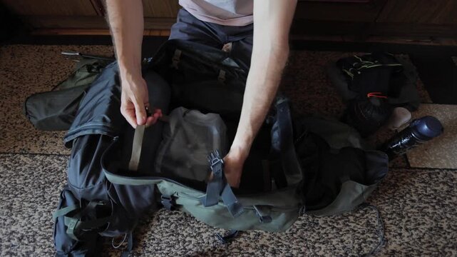 White man performing final check on travel backpack, methodical hands smoothing internal pocket, arranging essentials and sealing main compartment before stepping out