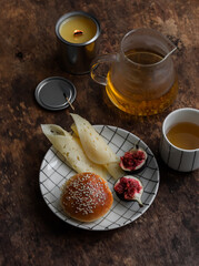 Cozy breakfast, snack - bun, cheese, figs, green tea and a candle on a wooden table