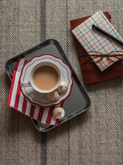 A cup of tea with milk, meringue on a metal tray, notebooks, glasses on the carpet, top view