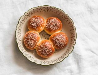 Sweet sesame buns in a baking dish on a light table, top view