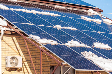Snow partially covers a roof mounted solar panel array on a brick building during winter.