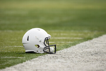 White Football helmet resting on the field of a football stadium. Copy space and good American...