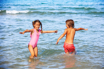 Summer at the beach. A happy girl and a boy are playing in the sea on a sunny day. The children raise their hands
