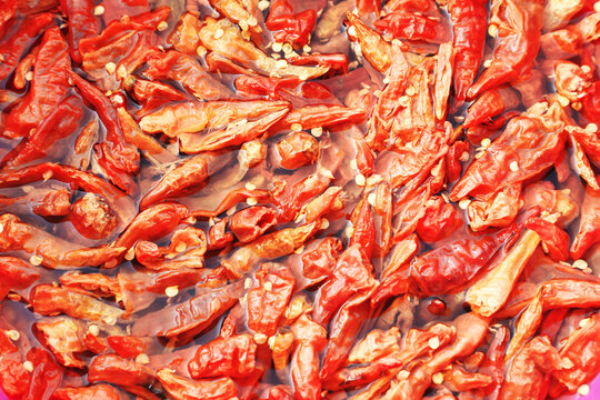An extreme close-up, top-down view of dried red chilies and seeds soaking in water, creating a vibrant and detailed food texture background.