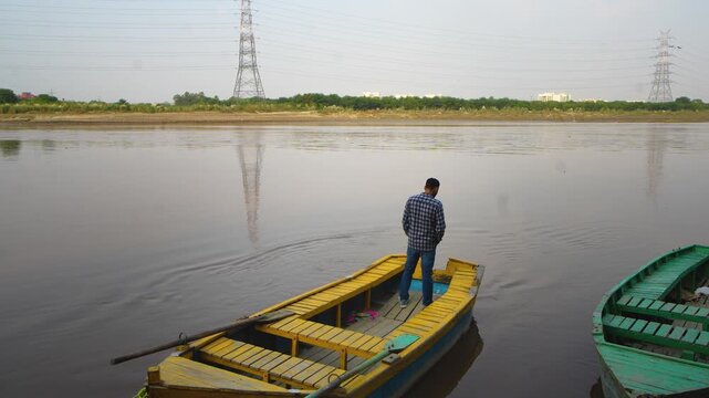 A man on a boat watching the Yamuna River at sunset along the banks in New Delhi, India &mdash; a peaceful aerial view of the river and golden evening sky.
