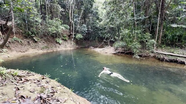 adventurous man swims in crystal clear pond hidden in lush dense rainforest, Licuala Forest Park, tropical North Queensland, near Cairns, Queensland, Australia