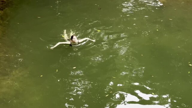 adventurous girl swims in crystal clear pond hidden in lush dense rainforest, Licuala Forest Park, tropical North Queensland, near Cairns, Queensland, Australia